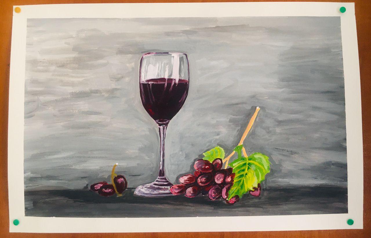 A glass of red wine beside a small bunch of grapes and a vine leaf on a muted grey ground